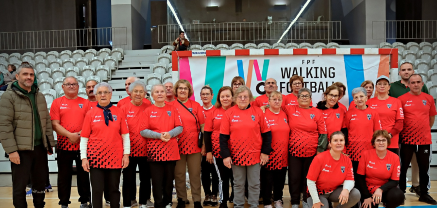 Grupo de mulheres em camisetas vermelhas, posando em frente a um banner de futebol.