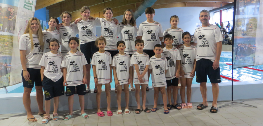 Grupo de crianças e adultos em t-shirts brancas, num ambiente de piscina.