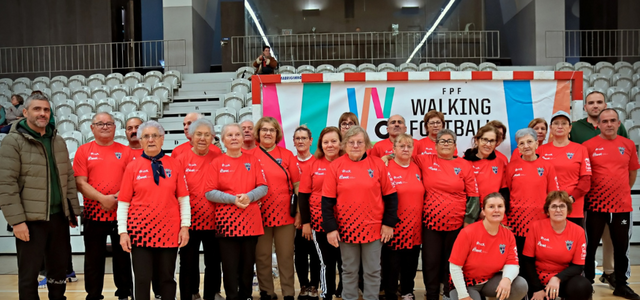 Grupo de mulheres em camisetas vermelhas, posando em frente a um banner de futebol.