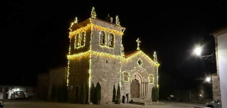 Igreja iluminada com luzes amarelas durante a noite, rodeada por árvores.